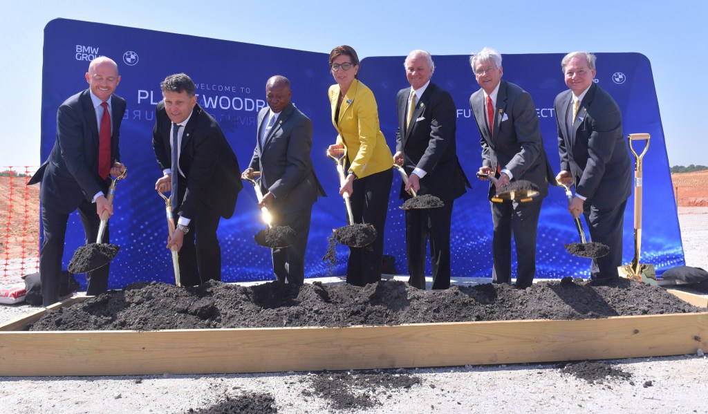 Executives and politicians in suits dig dirt with ceremonial shovels at a groundbreaking for a BMW battery plant in South Carolina.