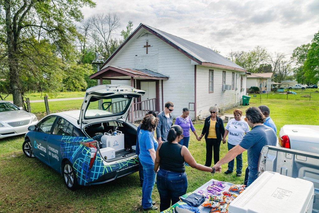 Pastor Harry Joseph leads community members, members of the Louisiana Environmental Action Network and Aclima scientist Aja Ellis in prayer on March 16, 2024 beside the Aclima air-monitoring car in front of the Mount Triumph Baptist Church in St. James Parish, La.